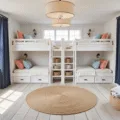 Photorealistic coastal-themed bunk room with natural morning sunlight, featuring white shiplap quad bunks, navy privacy curtains, cream linen bedding, coral and seafoam pillows, personalized wooden name plaques, vintage maritime decor, distressed oak ladder, jute area rug, and porthole-style mirrors.