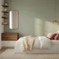 Photorealistic interior of a cozy small bedroom with soft golden hour lighting, featuring a queen-size platform bed with white linen and velvet pillows, a sage green accent wall, wooden nightstands, geometric shelving, and a gilt-edged mirror, showcasing clever storage solutions and minimalist decor.