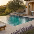 A luxurious Mediterranean outdoor kitchen and entertainment space featuring a 40ft infinity-edge pool at golden hour, with an L-shaped kitchen, cascading water feature, and ambient lighting.