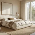 A serene modern beige bedroom featuring a king-sized bed with ivory linen bedding, bathed in soft morning light from floor-to-ceiling windows, complemented by lush textures and carefully curated decor.