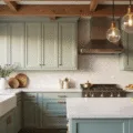 Photorealistic image of a luxurious modern farmhouse kitchen with sage green shaker cabinets, vintage brass hardware, and a white quartz waterfall island, illuminated by golden hour sunlight.
