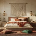 A sunlit boho bedroom featuring a low-profile bed with layered textiles, a macramé wall hanging, scattered jewel-toned cushions, and abundant plants, all illuminated by warm string lights and paper lanterns.