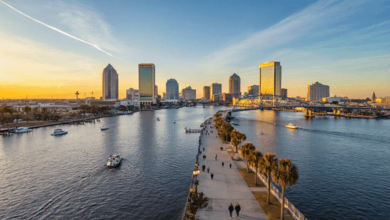 Jacksonville in January: Your Ultimate Winter Escape Guide (Without the Freezing Temps!) "Aerial view of Jacksonville, Florida featuring the St. Johns River, Main Street Bridge, and downtown skyline during a sunset in January, with people strolling along the Riverwalk and boats on the water."