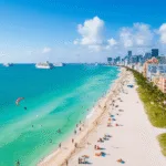 "Aerial view of Miami Beach with Art Deco buildings, palm trees, colorful beach umbrellas, hotel pools, yachts, and beachgoers on a sunny day"