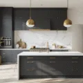 Photorealistic interior of a modern minimalist kitchen featuring charcoal gray lower cabinets, a white quartz waterfall island, a dramatic marble backsplash, and industrial brass pendant lights, illuminated by morning sunlight and showcasing curated ceramics on floating metal shelves.