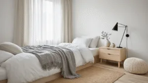 Small Guest Bedroom Ideas: Transform Your Tiny Space into a Cozy Retreat A serene Scandinavian guest bedroom featuring a twin bed with crisp white linens, soft gray throws, light blonde wood nightstand, a ceramic lamp, and natural light filtering through sheer linen curtains, set on a light wooden floor with a jute rug and knitted cream pouf.