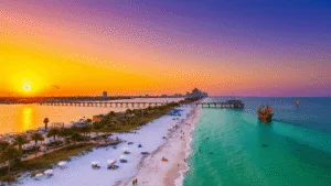 Escape to Paradise: The Ultimate Clearwater Adventure Guide You Can't Miss "Aerial view of Clearwater Beach at sunset with Pier 60, palm trees, white umbrellas, dolphins, parasailers, beachgoers, a pirate ship cruise, and Clearwater skyline"