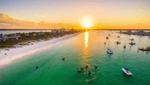 🏖️ Insider's Guide: Discover the Most Epic Fun Things to Do in Destin, Florida "Dramatic drone shot of Destin's coastline at sunset, showcasing emerald-green waters, pristine sandy beaches, Henderson Beach State Park's boardwalk, parasailers, dolphins, fishing boats, and HarborWalk Village with beachside activities and water sports."