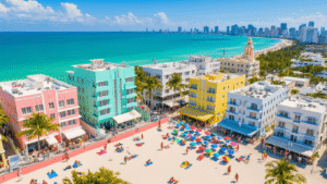 South Beach Miami August: Your Ultimate Guide to Sun, Sand, and Sizzling Summer Adventures "Aerial view of a vibrant South Beach Miami in summer with pastel Art Deco buildings, bustling beach activities, colorful lifeguard towers, and the city skyline under a bright blue sky"